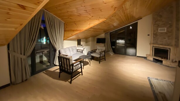 A cozy attic room with a wooden ceiling, a fireplace, and a seating area with a sofa and chairs.