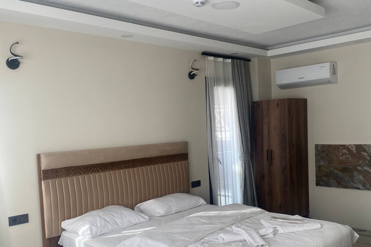Ein modernes Schlafzimmer mit einem großen Bett, einem Nachttisch aus Holz, einem Kleiderschrank und einer Klimaanlage an der Wand.