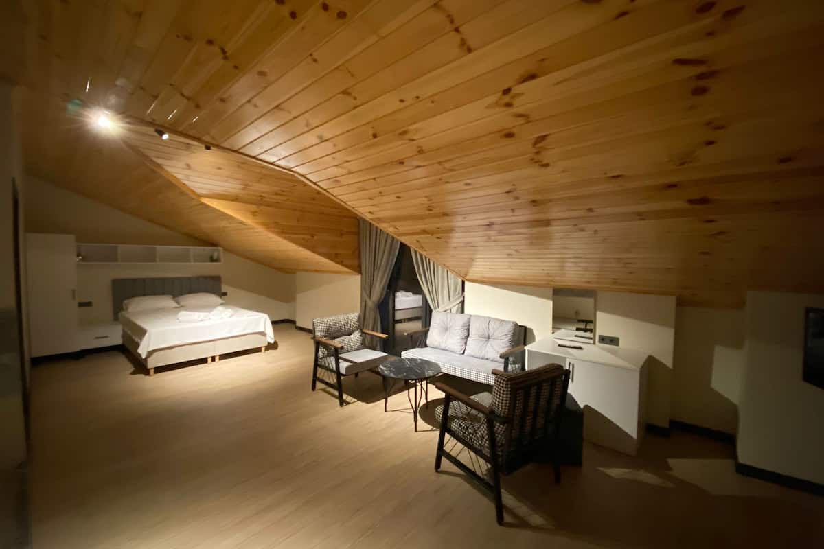 Ein gemütliches Schlafzimmer im Dachgeschoss mit Holzbalkendecke, einem Bett, einer Couch und einem Esstisch.