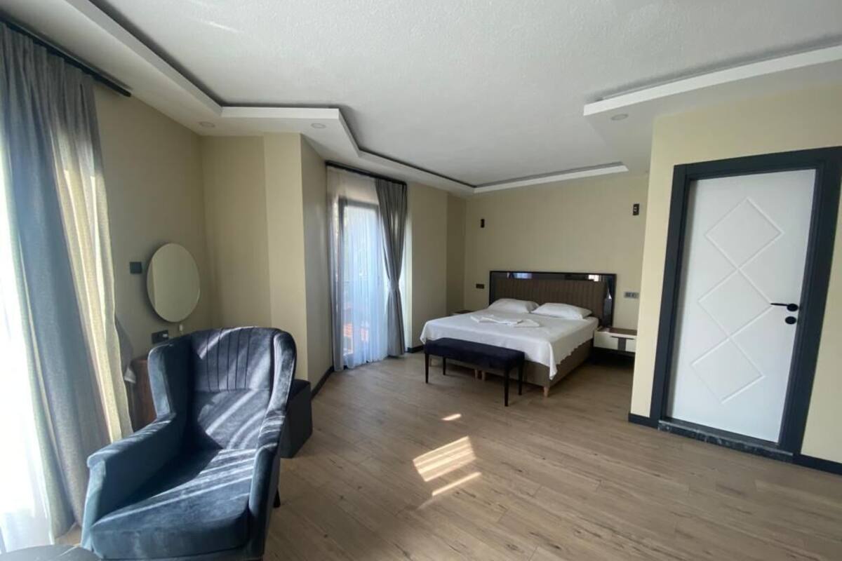 Ein Hotelzimmer mit Bett, Sessel, Nachttisch, Spiegel und Tür.