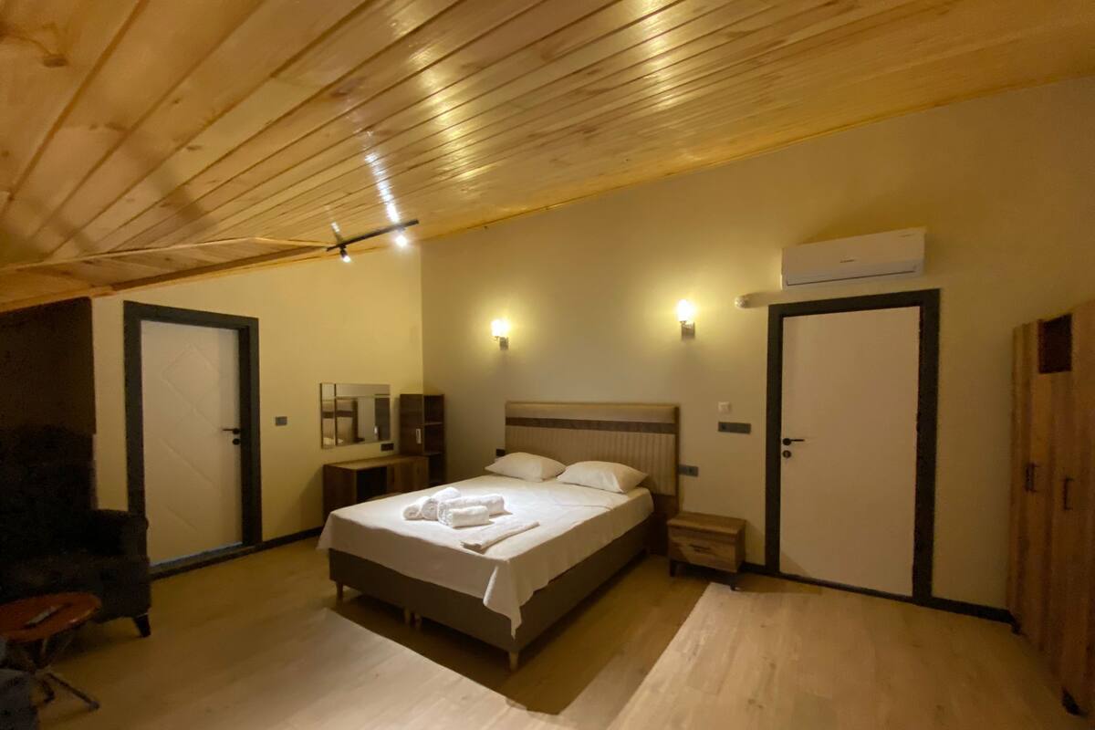 Ein Schlafzimmer mit Holzboden, einem Bett mit weißer Bettwäsche, zwei Nachttischen, einem Schminktisch und einer Klimaanlage.