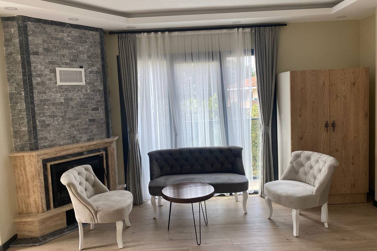 Ein Wohnzimmer mit Kamin, zwei Sesseln, einer Couch und einem Holzschrank.