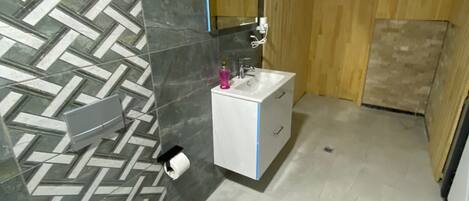 A bathroom with a white sink, a mirror above it, and a toilet. The walls have a herringbone pattern, and there is a wooden panel on one side.