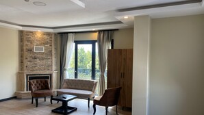 A modern living room with a fireplace, two sofas, a coffee table, and a view of greenery outside.