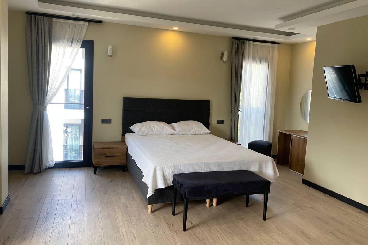 Ein Hotelzimmer mit einem Bett, einer Sitzbank, einem Fernseher und einem Vorhangfenster.