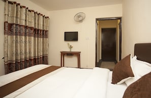 A hotel room with a bed, a bedside table with a vase of flowers, a wall-mounted TV, and a door leading to another room. - OYO 209 Tibet Peace Inn (Kathmandu)