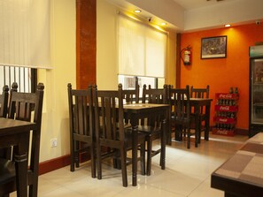 A restaurant with wooden tables and chairs, a fire extinguisher on the wall, and a Coca-Cola cooler. - OYO 209 Tibet Peace Inn (Kathmandu)
