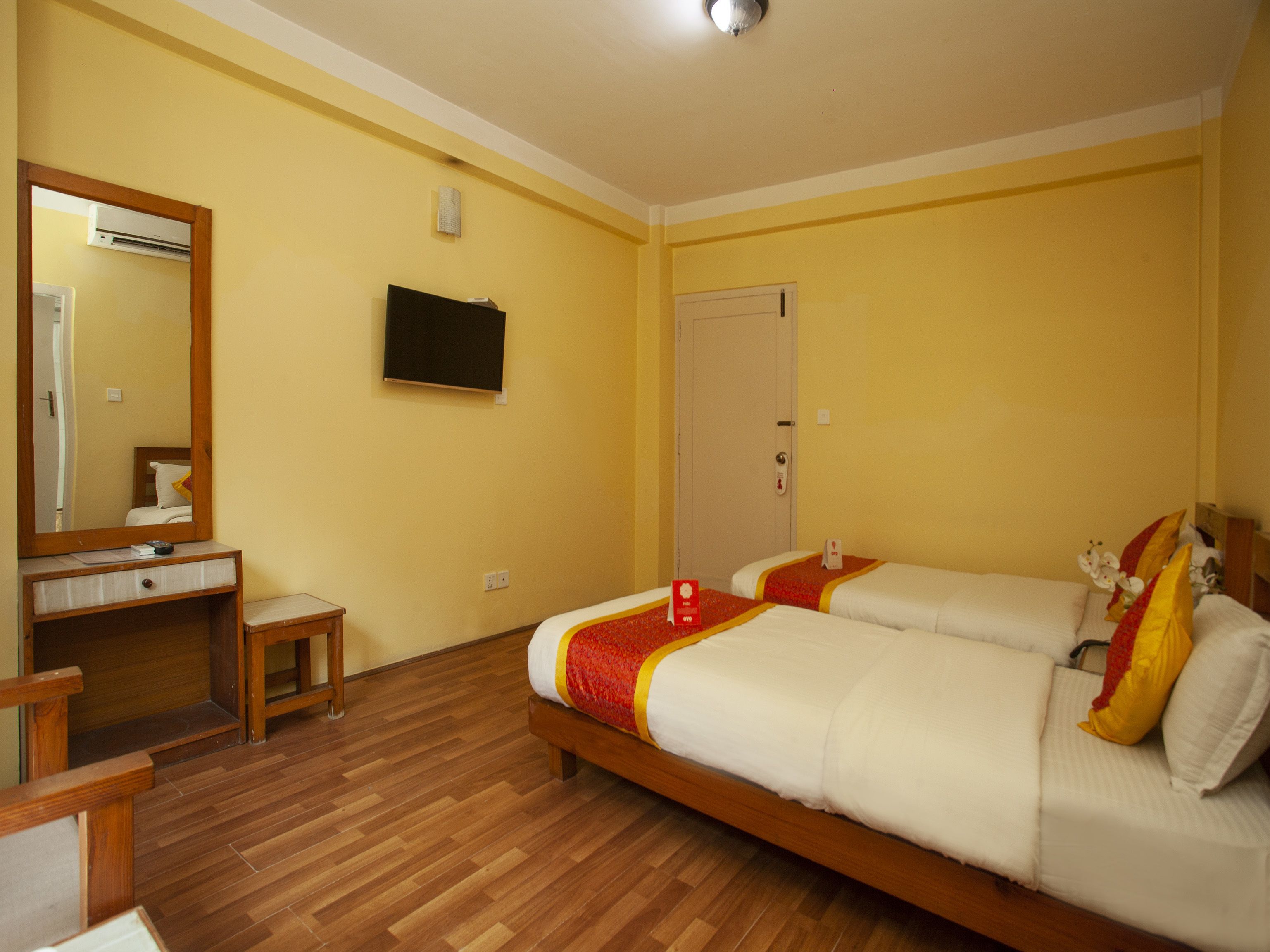 A hotel room with two beds, a wooden desk, a mirror, a television, and a door.