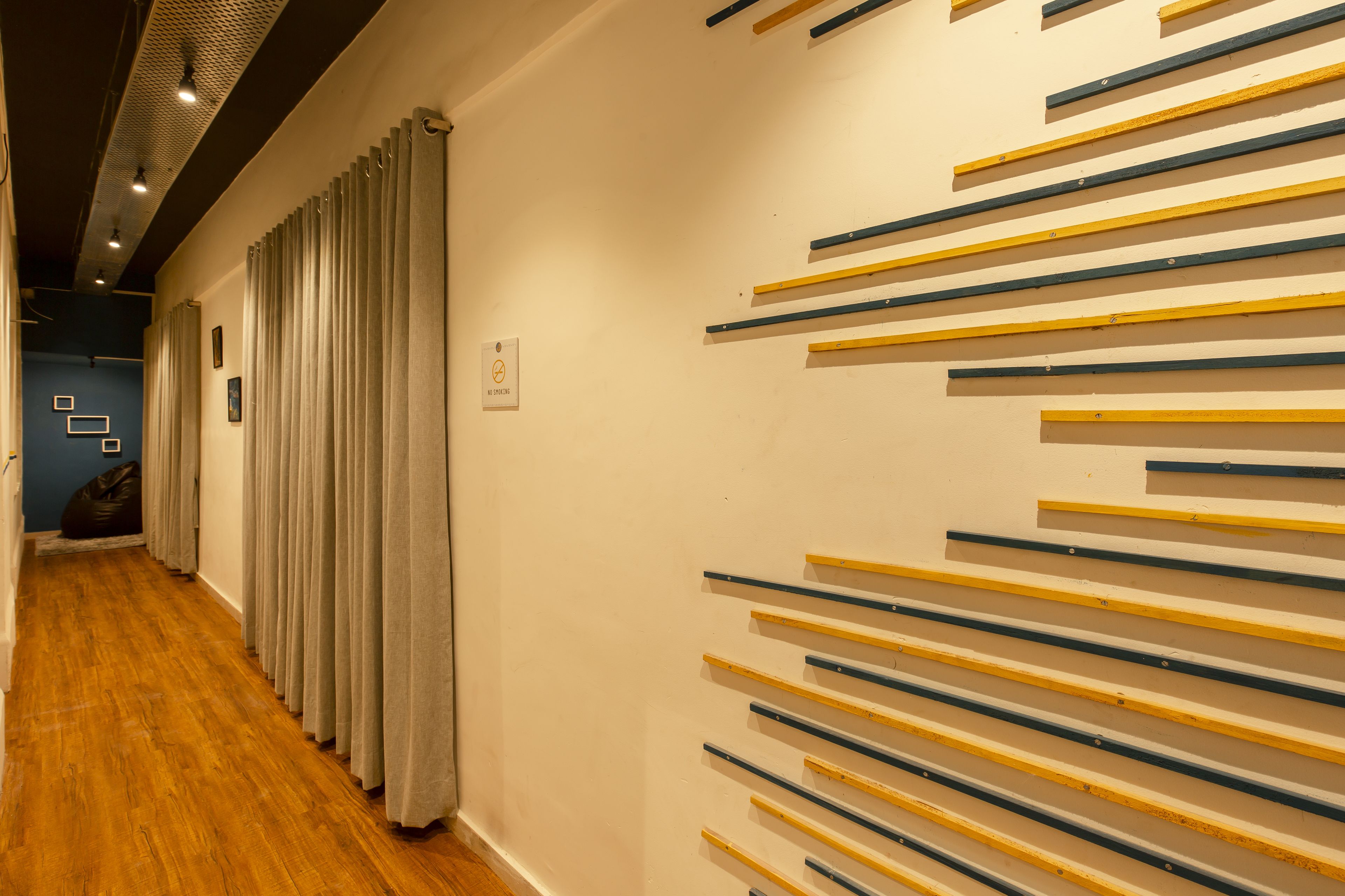 A hallway with wooden flooring, a row of curtains on the left, and a wall with horizontal wooden planks.