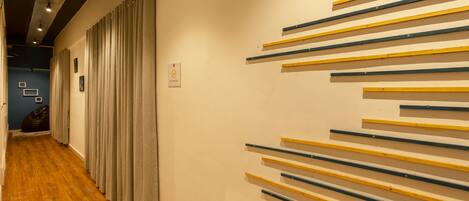 A hallway with wooden flooring, a row of curtains on the left, and a wall with horizontal wooden planks.
