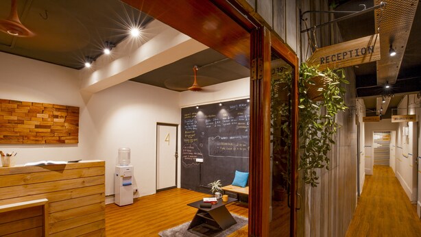 A reception area with a wooden reception desk, a water dispenser, a chalkboard with writing, and a sign indicating the reception. - Locomo Hostel OG - Stay Work Eat (Mumbai)