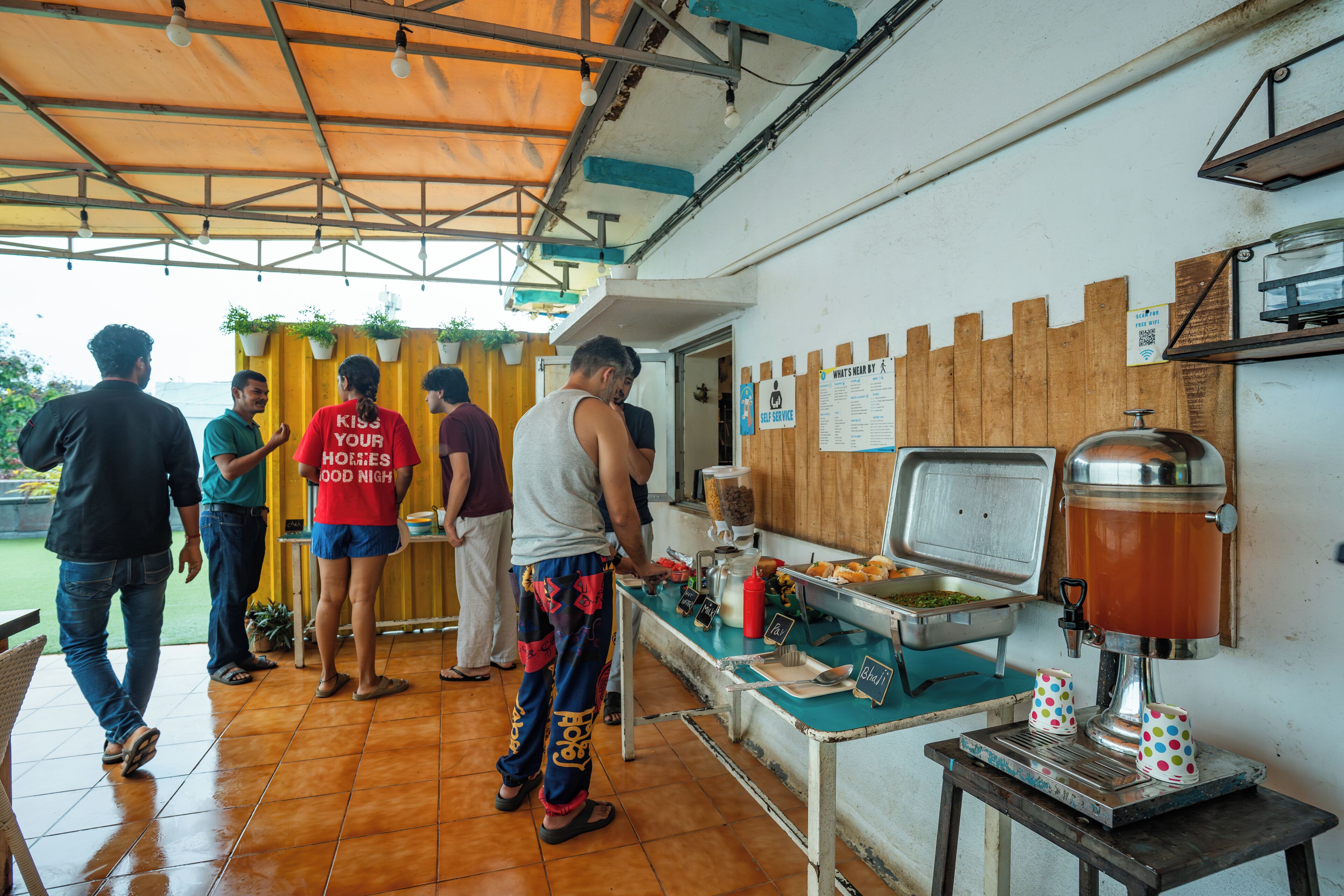 Zona de comida con una máquina de café, una mesa de buffet y un letrero que indica servicio propio.