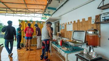 Zona de comida con una máquina de café, una mesa de buffet y un letrero que indica servicio propio.