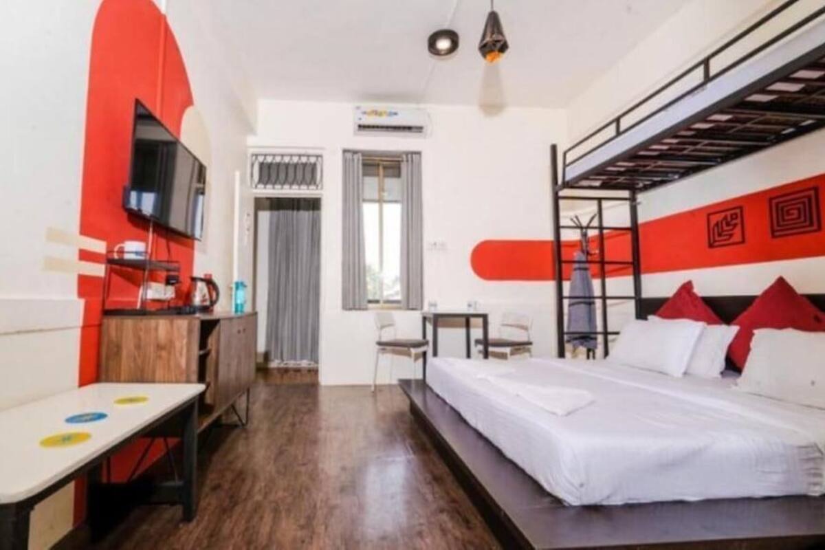A compact hotel room with a bunk bed, a desk with a chair, a small table, and a television.