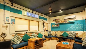 A cozy, modern lounge area with a large window, wooden furniture, and a sign reading "LOCCREAT". - Locomo Hostel OG - Stay Work Eat (Mumbai)