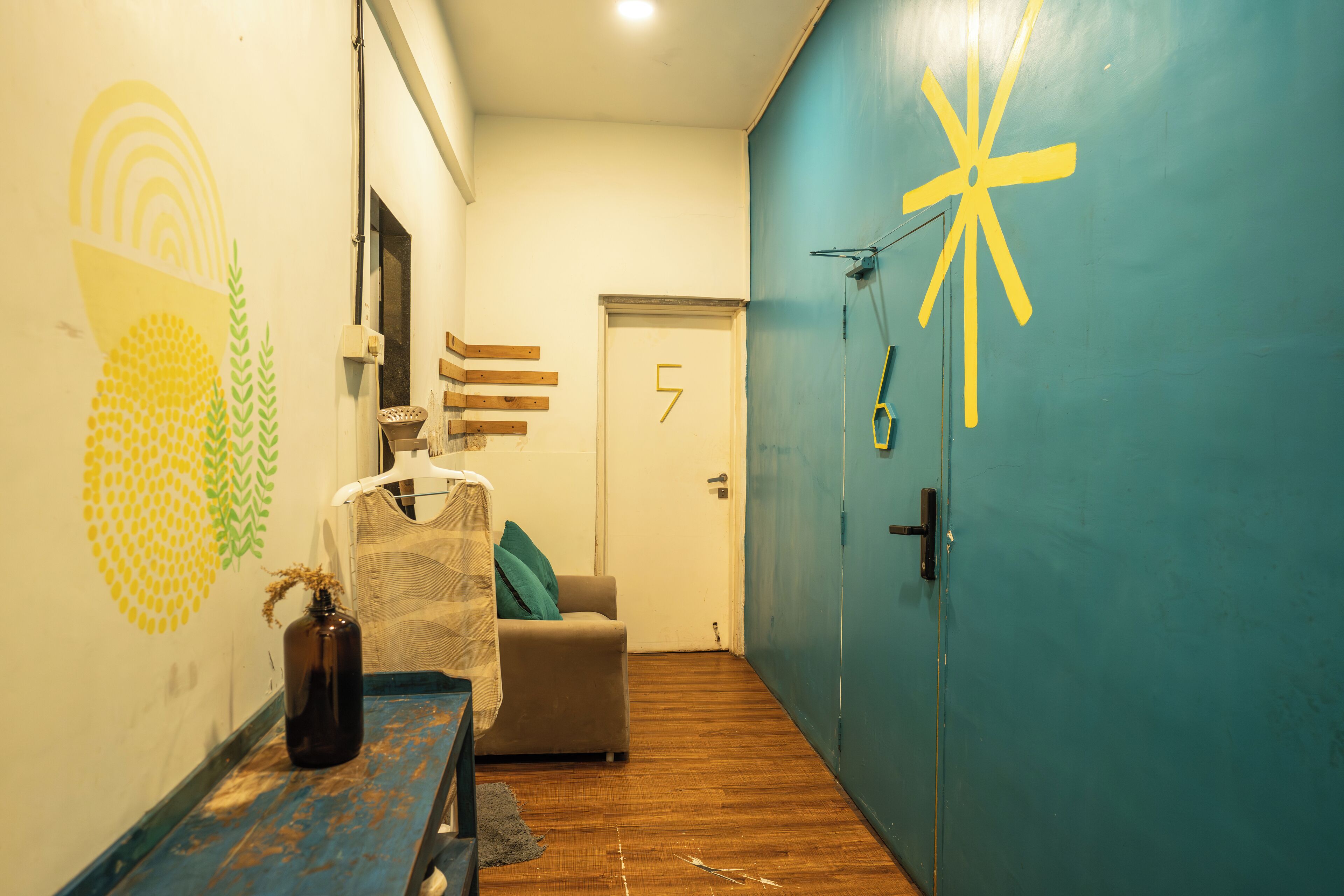 A hallway with a blue door, a wooden bench, a small table with a bottle, and a chair.