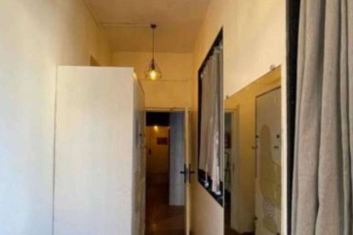A narrow hallway with a trash bin, a hanging light fixture, and a door at the end.