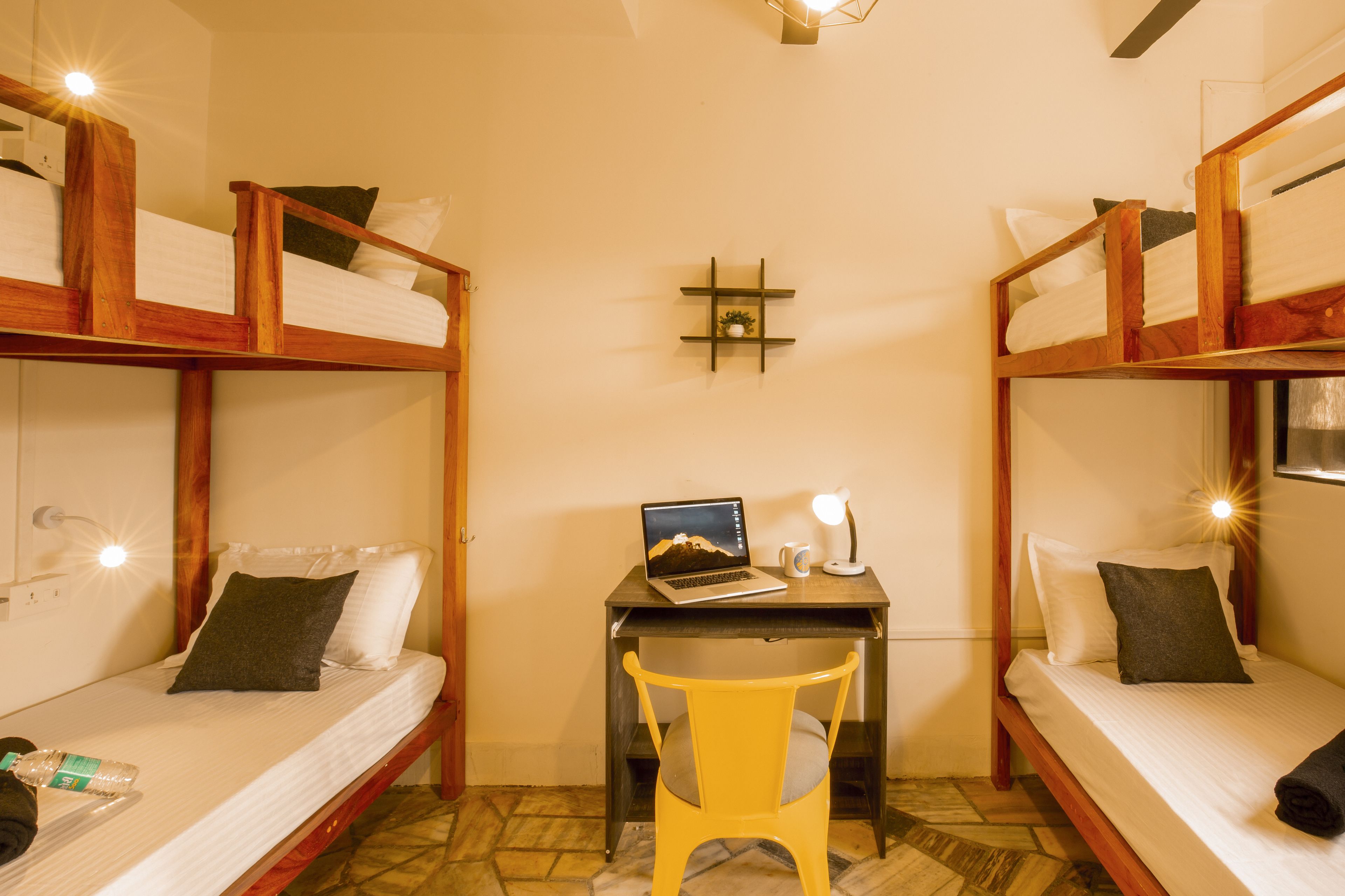 Quarto com duas camas de solteiro sobrepostas, uma mesa com um laptop e uma cadeira.