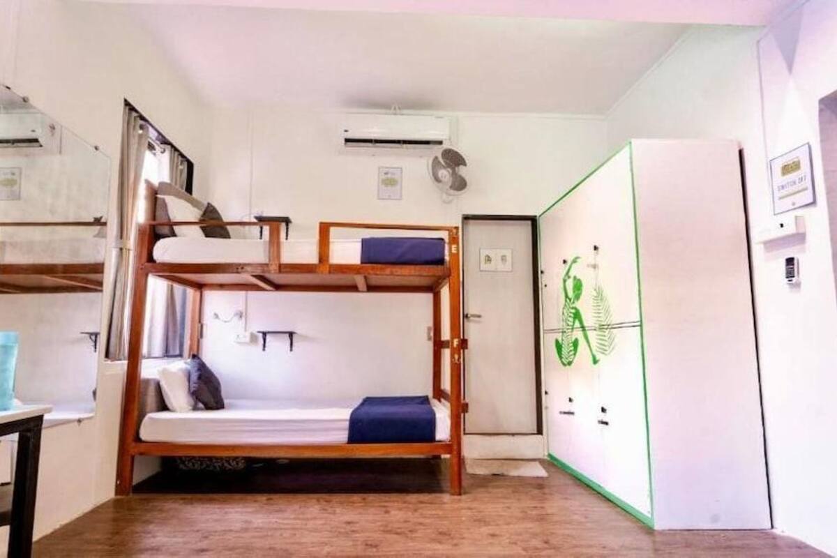 A bunk bed room with a desk, a mirror, and a refrigerator.