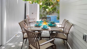 An outdoor dining area with a table set for four, surrounded by wicker chairs, with a view of a pool and palm trees.