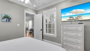 A bedroom with a bed, a television mounted on the wall, a dresser, and a door leading to another room. - **THE TOASTED COCONUT @ OLD TOWN** Pool + Last Key White Glove Service... (Key West)