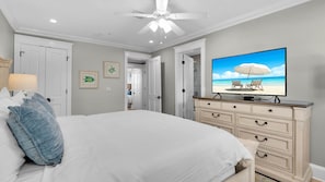 A bedroom with a bed, a dresser, a television displaying a beach scene, and a ceiling fan.