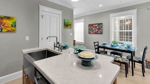 A kitchen with a marble countertop, a sink, and a dining area with a table set for two.