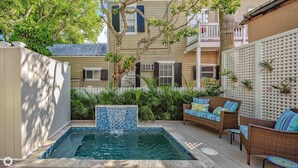 Un jardin avec une piscine, des meubles en osier et une clôture blanche.