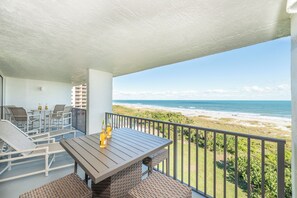 Ein Balkon mit Korbmöbeln, einem Holztisch und Flaschen.