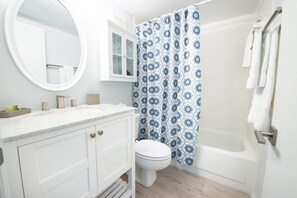 Ein Badezimmer mit einem weißen Waschtisch, Toilette, Badewanne und einer Duschvorhang mit blau-weißen Mustern.