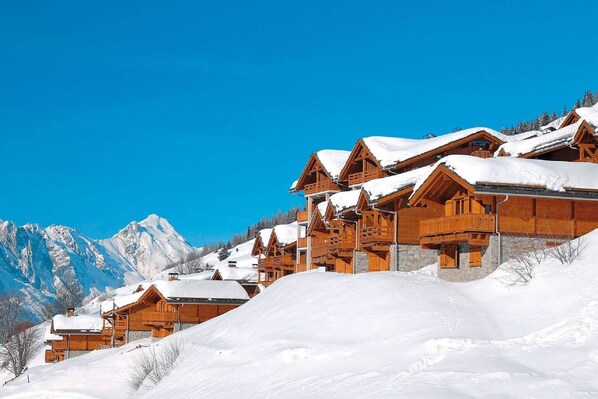 Un albergue de montaña cubierto de nieve con arquitectura de madera y un cielo azul despejado.