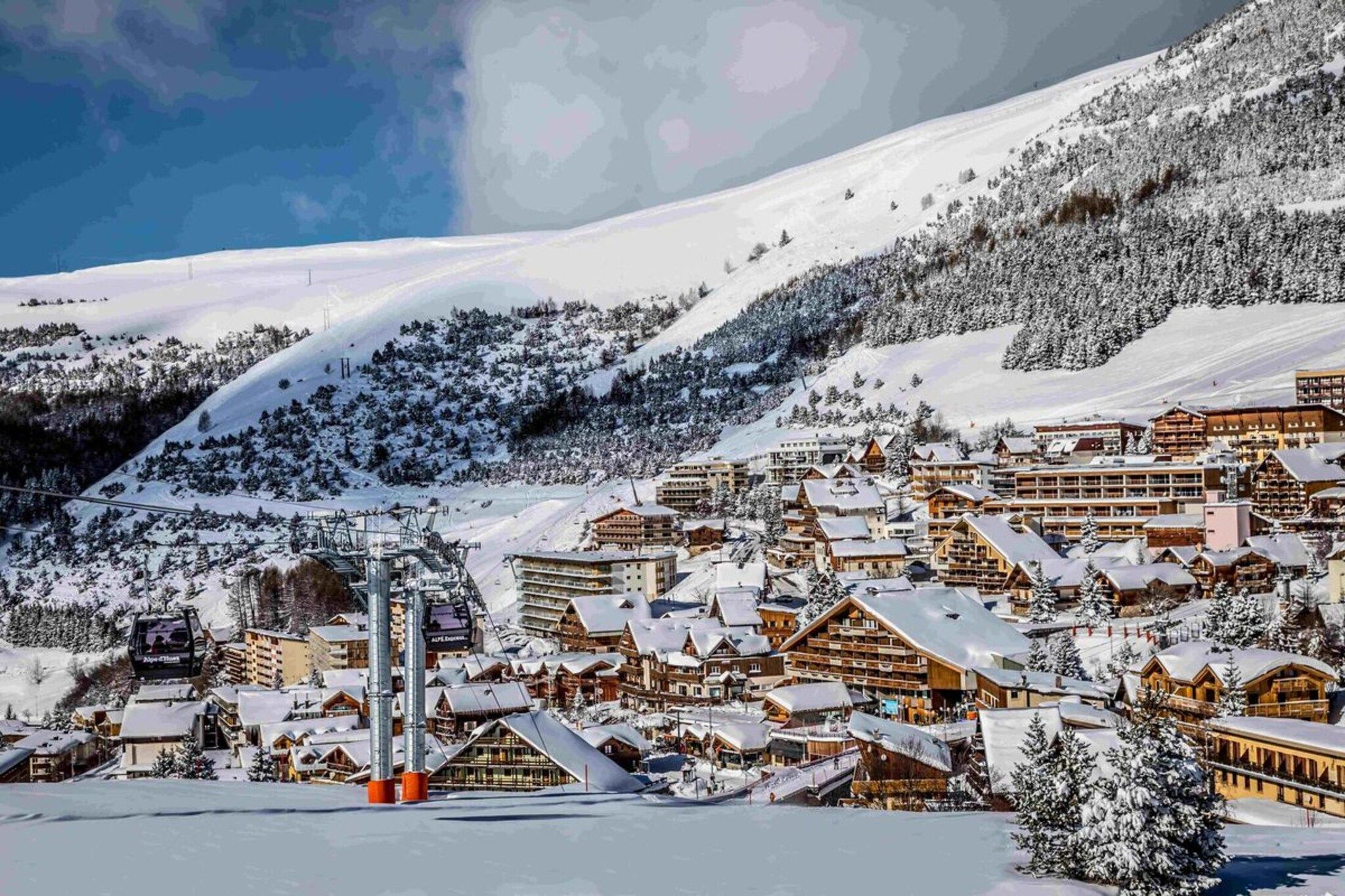 Eine verschneite Bergstadt mit Holzhäusern, einer Seilbahn und wolkenlosem Himmel.