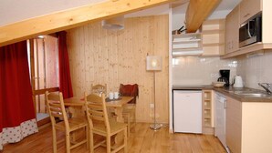 A compact kitchen with wooden flooring, a dining table with chairs, a refrigerator, a microwave, and a sink. - Chalet in French Alps with Scenic Views (VALMEINIER)