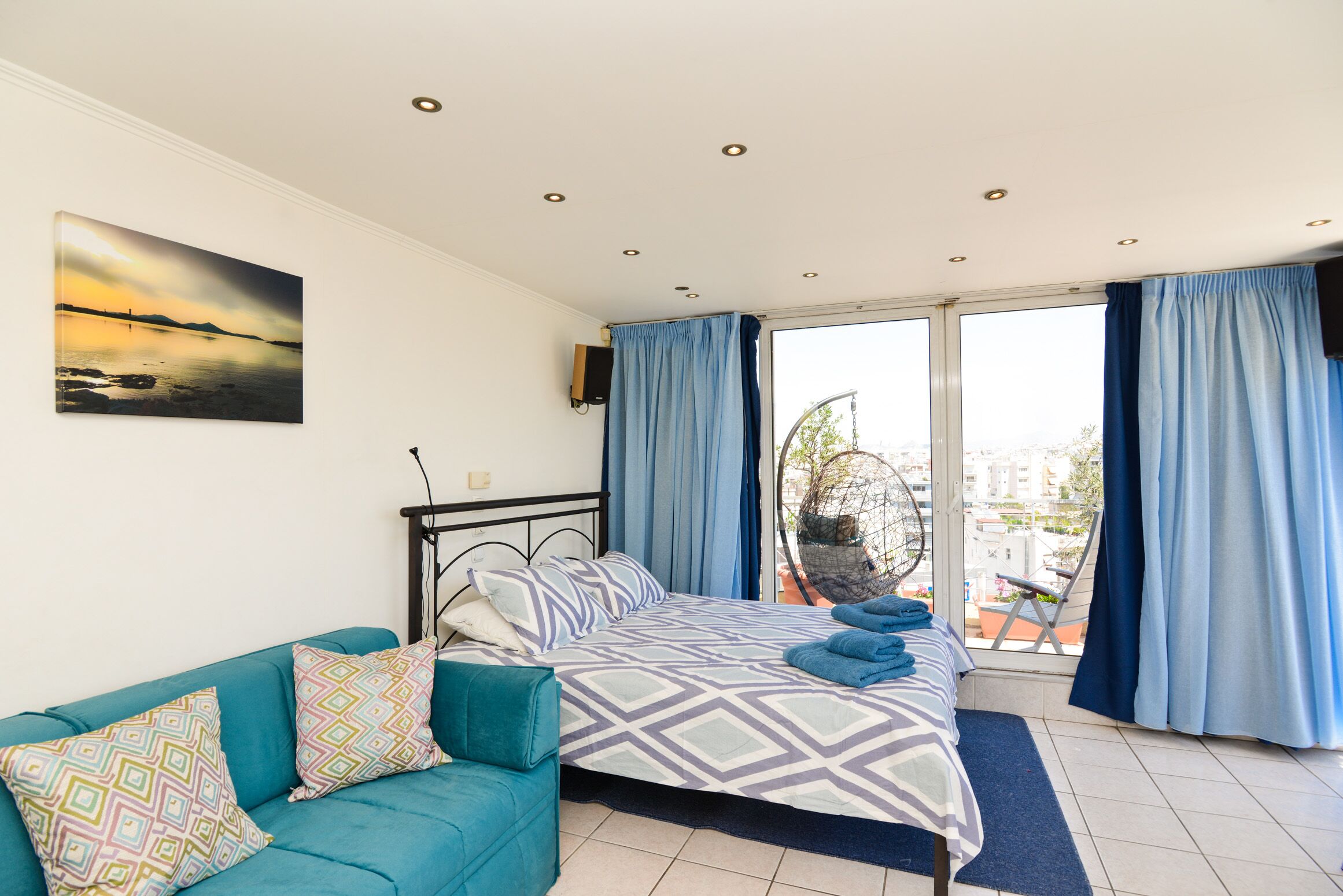 A bedroom with a bed, a sofa, and a balcony with curtains.