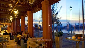 Un ristorante sul lungomare con posti a sedere all'aperto, ampie finestre e vista sull'acqua.