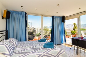 A bedroom with a bed, curtains, a hanging chair, a table, and a view of the city. - Athens Panoramic Top floor view private terrace (Paleo Phaliro)