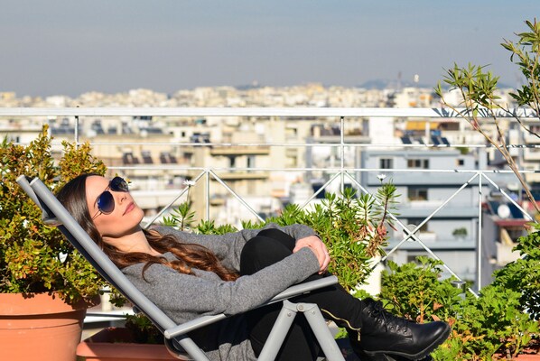 A person reclining on a chair with a cityscape in the background. - Athens Panoramic Top floor view private terrace (Paleo Phaliro)