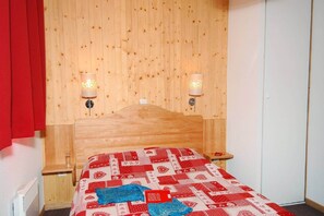 Ein Zimmer mit einem hölzernen Kopfteil, zwei Nachttischlampen, einer roten und weißen Bettdecke und einem roten Vorhang.