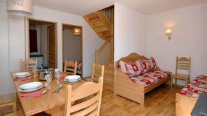 Una stanza accogliente con un tavolo da pranzo per quattro persone, un letto di legno con coperta fantasia e una scala in legno, oltre a un lampadario fissato al muro.