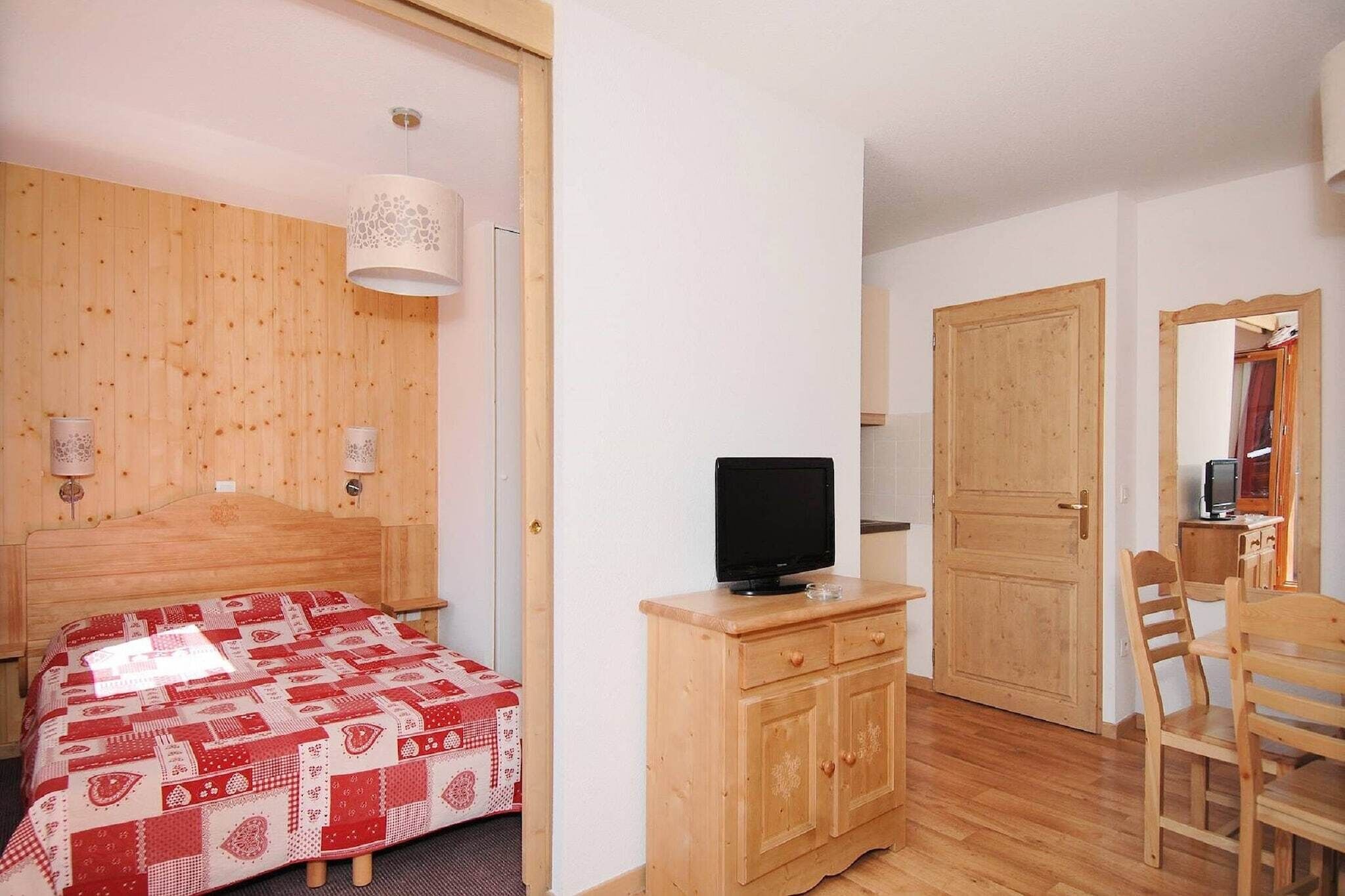 A bedroom with a bed, a TV on a wooden dresser, a wooden wardrobe, and a door.