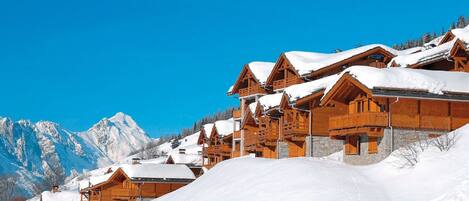Een bergchalet bedekt met sneeuw, met houten architectuur en een helderblauwe lucht.