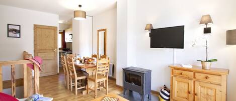A cozy living room with a wooden dining table, chairs, a TV, and a wood-burning stove.