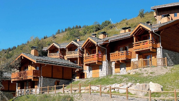 Filas de cabañas de madera con cimientos de piedra y balcones de madera, bajo un cielo despejado.