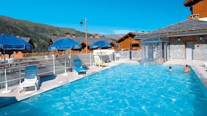 Una piscina con sillones de descanso y sombrillas, rodeada de edificios de madera y un paisaje montañoso.