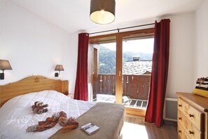 A bedroom with a bed, a wooden dresser, a nightstand, two wall lamps, and a window with red curtains. - Apartment with dishwasher, in Valmeinie (VALMEINIER)