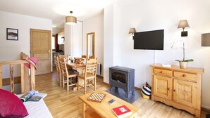 Uma sala de estar acolhedora com uma mesa de jantar de madeira, cadeiras, uma TV e uma lareira a lenha.