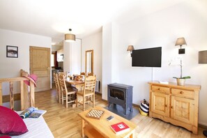 A cozy living room with a wooden dining table, chairs, a TV, and a wood-burning stove. - Apartment with dishwasher, in Valmeinie (VALMEINIER)