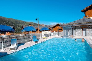 A swimming pool with lounge chairs and umbrellas, wooden cabins, and a mountainous backdrop. - Apartment with dishwasher, in Valmeinie (VALMEINIER)