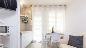 Una cucina compatta con mobili bianchi, un forno a microonde e un'area pranzo con tavolo e sedie.
