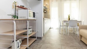 Una cucina moderna con forno a microonde, macchina da caffè e una piccola pianta su uno scaffale. C'è un'area pranzo con tavolo e sedie, e un divano nel soggiorno.